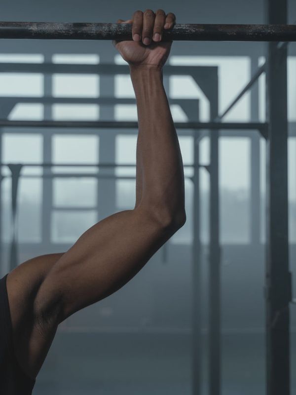 Close-up of a man's hands gripping a pull-up bar, muscles tense.